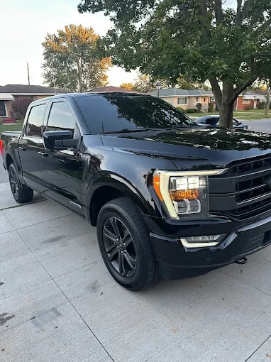 Black Ford F-150 pickup truck parked on concrete driveway with trees
