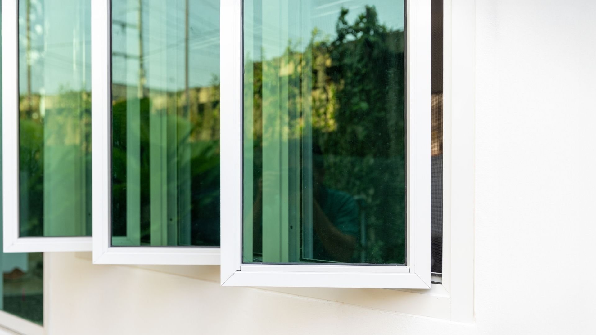 White-framed windows with green-tinted glass reflecting trees and sky